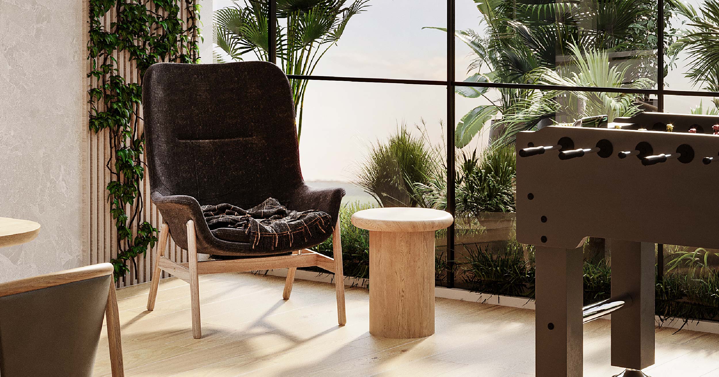 Westwood By Imtiaz Modern interior featuring a cozy chair, round wooden table, greenery, and a foosball table by large windows.